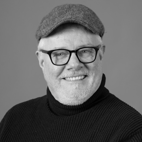 Peter Isaksson Portrait of elderly man with glasses, cap and black sweater, smiling.