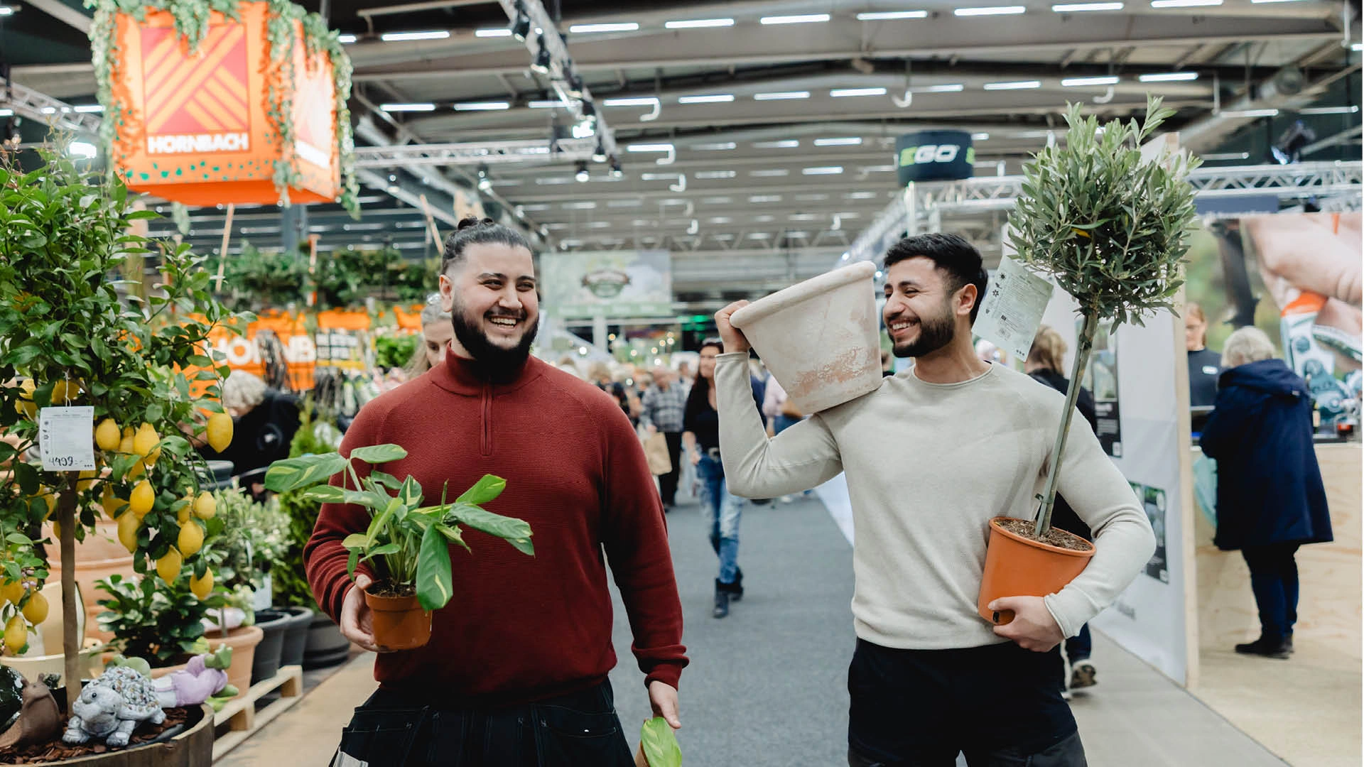 webb bild-3_4 Två personer promenerar i mässgång med krukväxter i händerna.