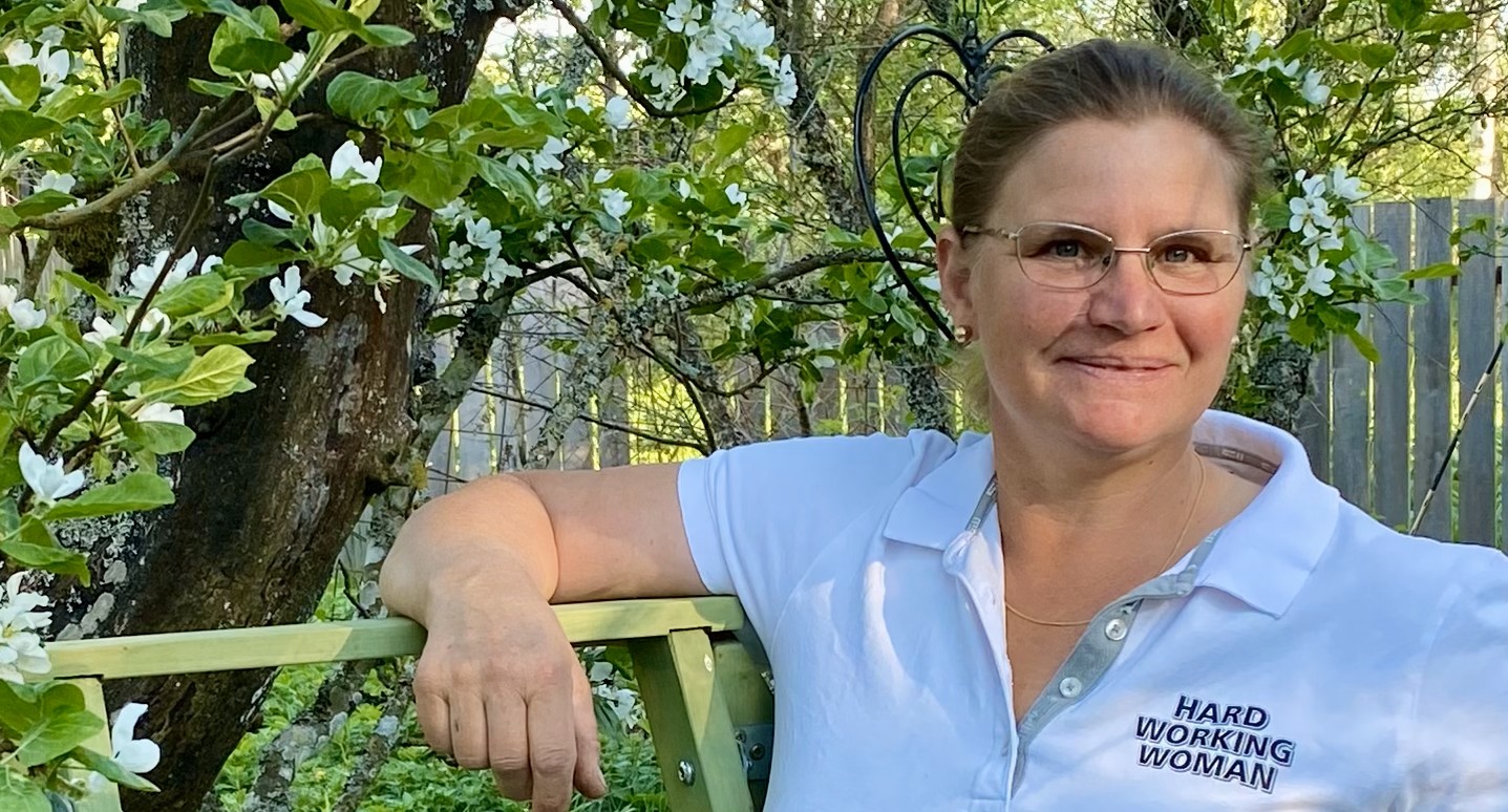 Eva o stege 2 En kvinna står ute i en trädgård med blommande äppelträd i bakgrunden